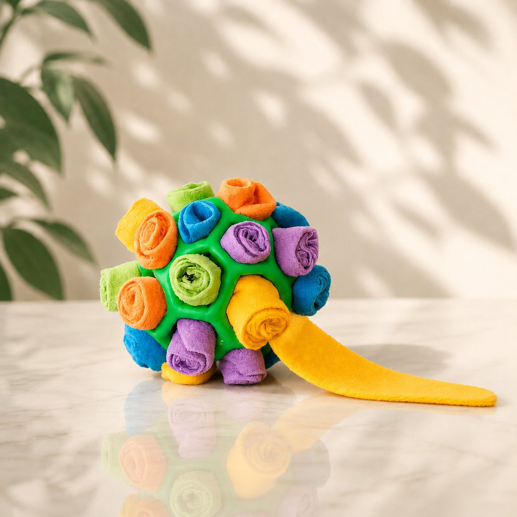 Colorful fleece snuffle ball with green rubber core and hidden treats, dog sniffing it on floor (view 2)