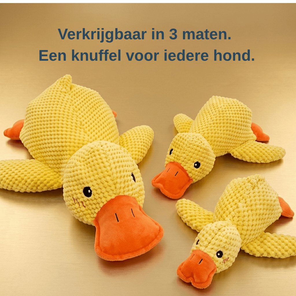 Yellow plush duck dog toy with orange bill and feet, textured fabric, lying on a light surface (view 4)