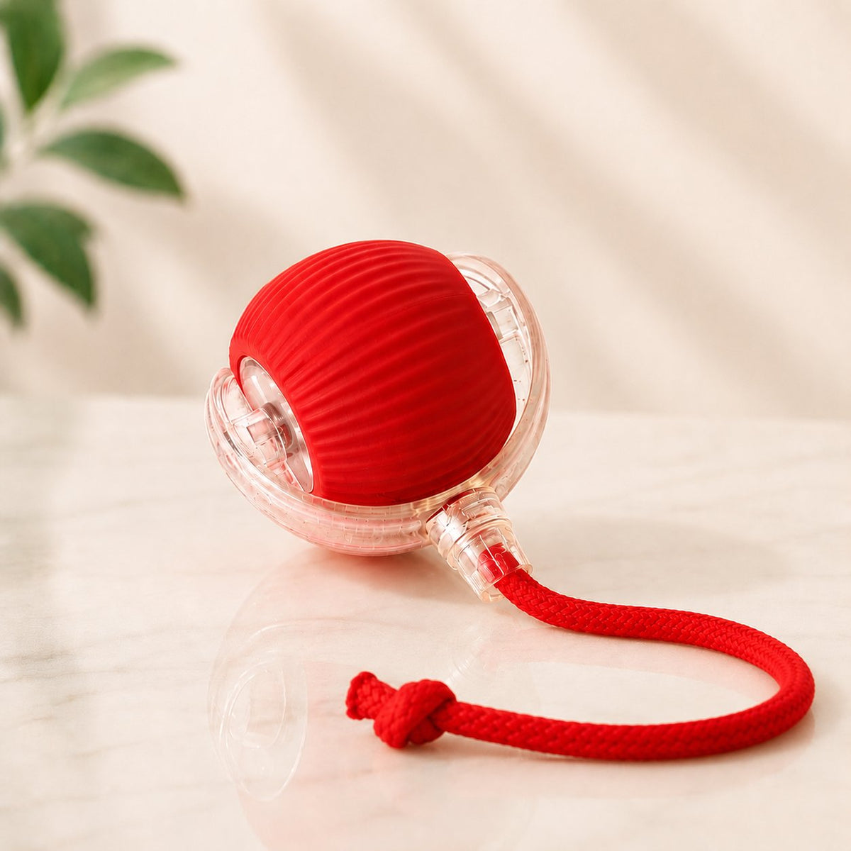 Red silicone interactive rolling pet ball with braided rope tail, shown with a cat playing indoors (view 2)